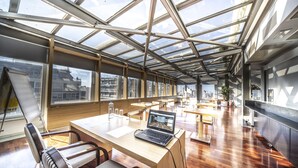 Ein moderner Arbeitsraum mit Glasdecke, Holztischen und -stühlen sowie ein Laptop auf einem der Tische.