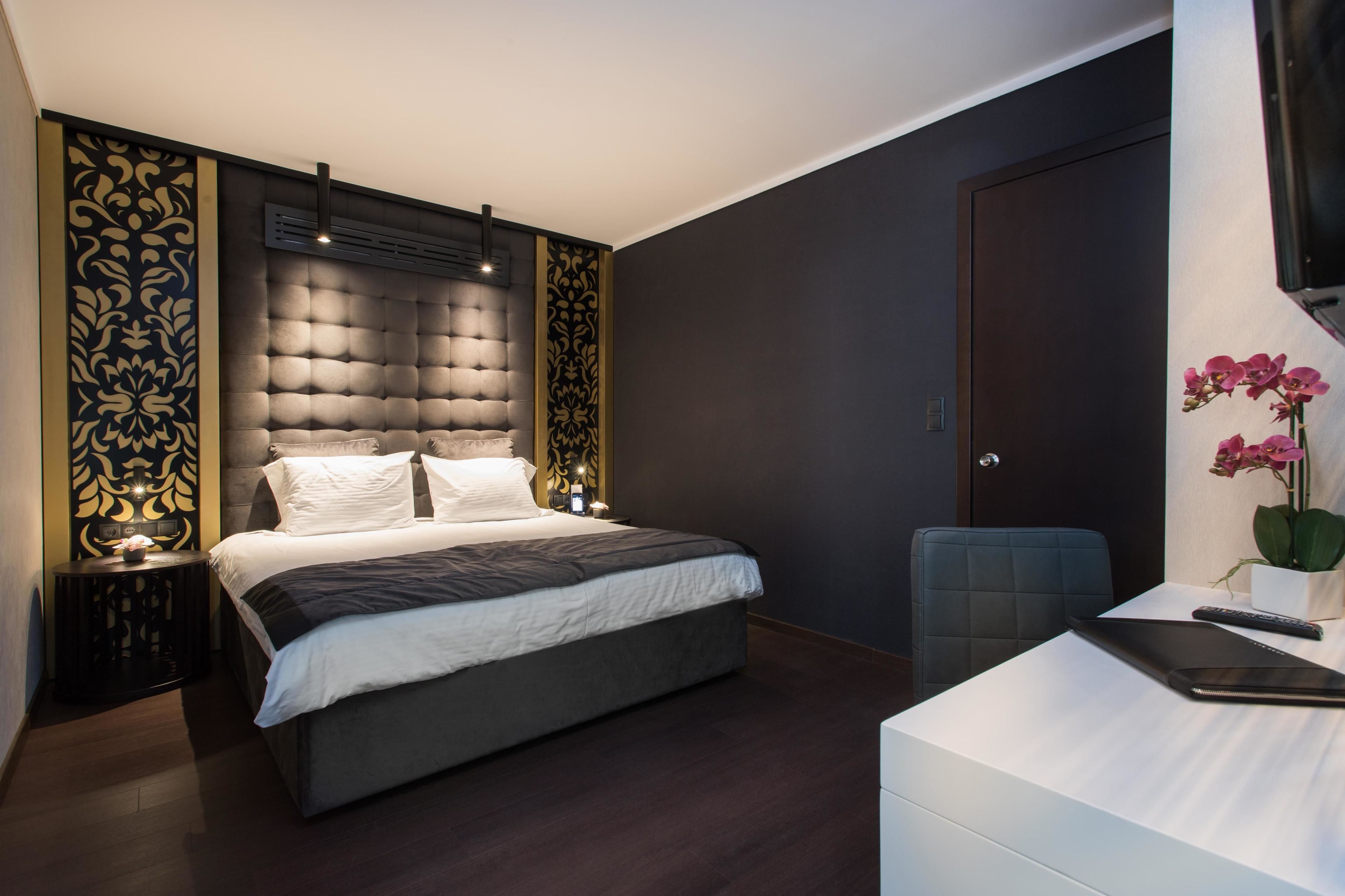 A modern bedroom with a tufted headboard, a white bed, a desk with a laptop, and a TV on the wall.