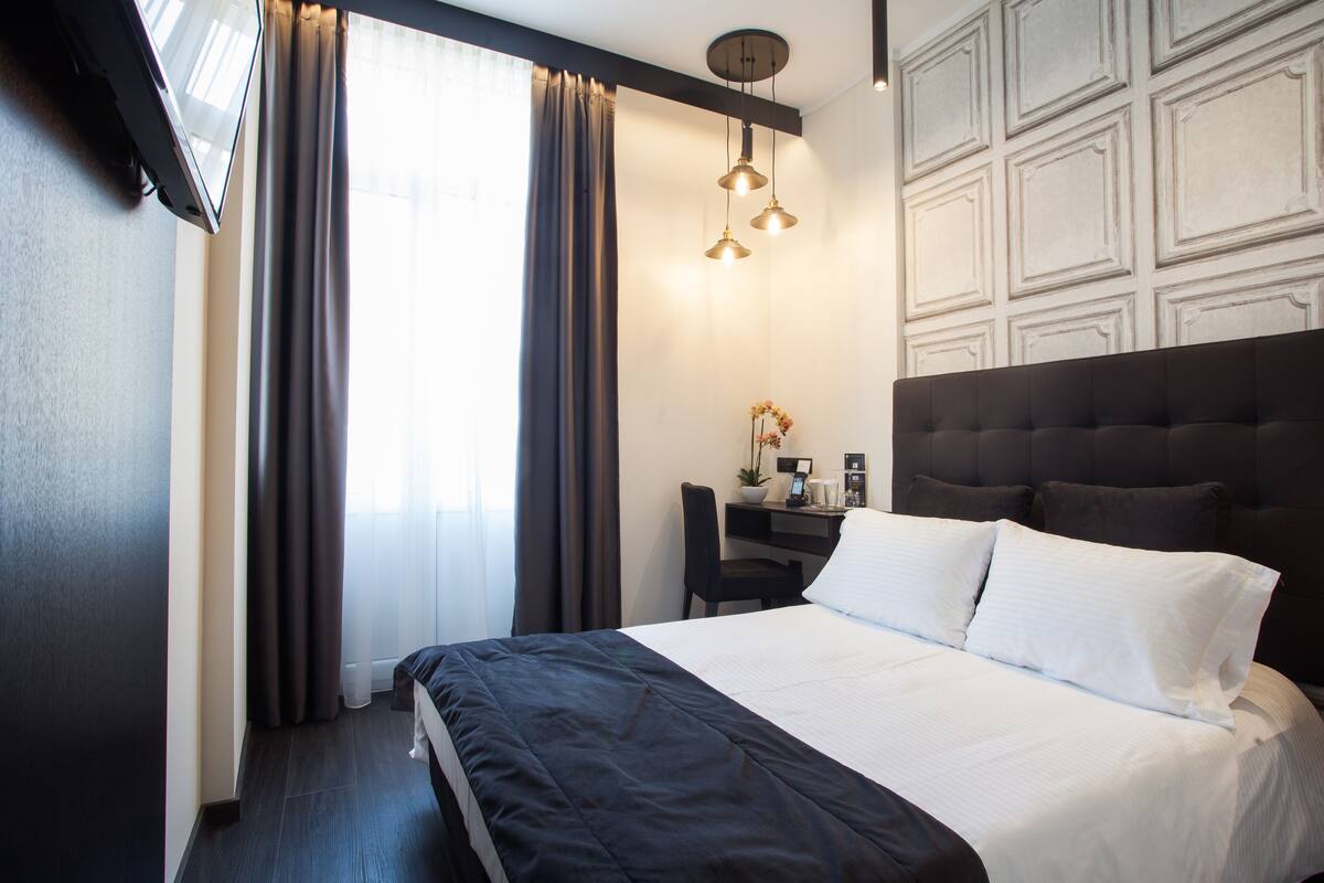 Ein Hotelzimmer mit einem großen Bett, einem Schreibtisch mit Computer und einem Stuhl.