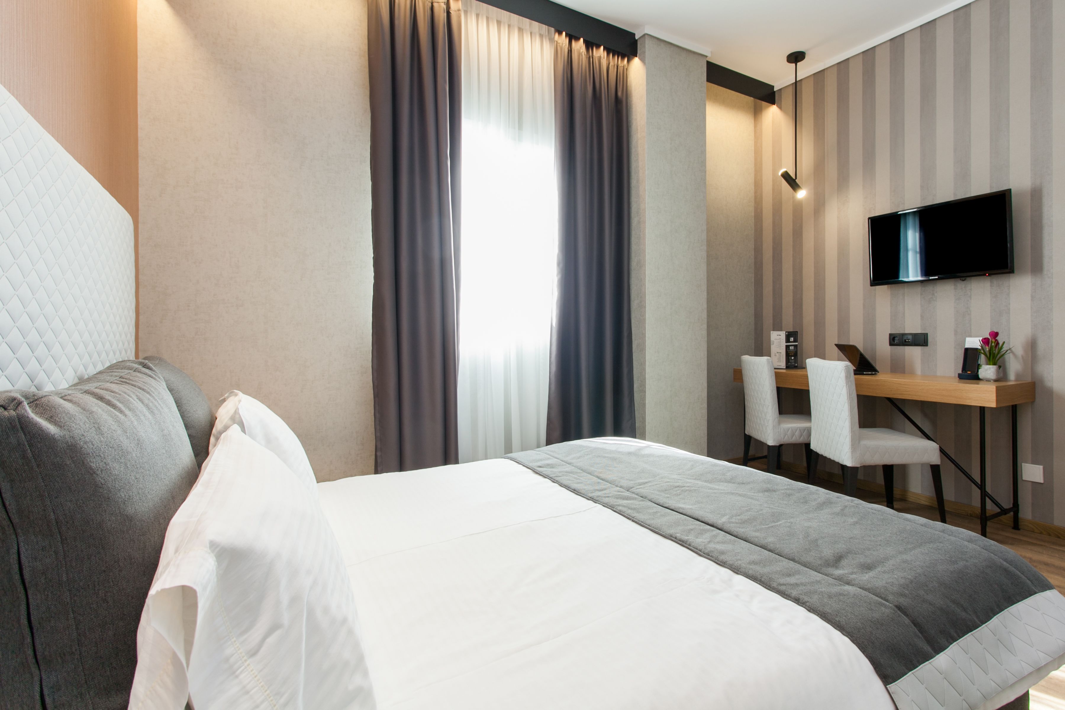 A hotel room with a bed, a desk, two chairs, a TV, and a window with curtains.