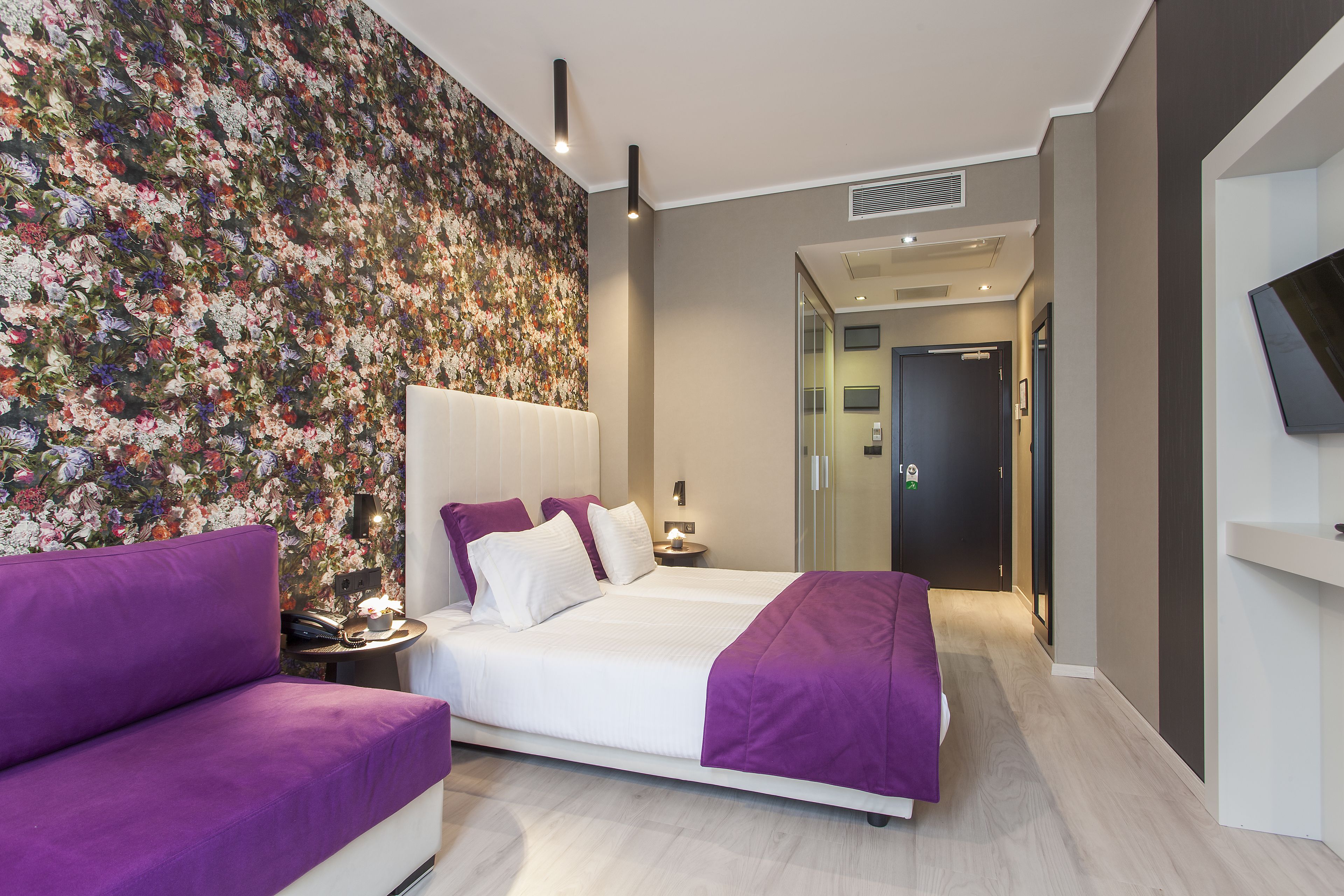 A modern bedroom with a large bed, a sofa, and a floral wallpaper.