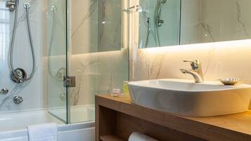 Un baño moderno con ducha acristalada, lavamanos blanco y tocador de madera con toallas.