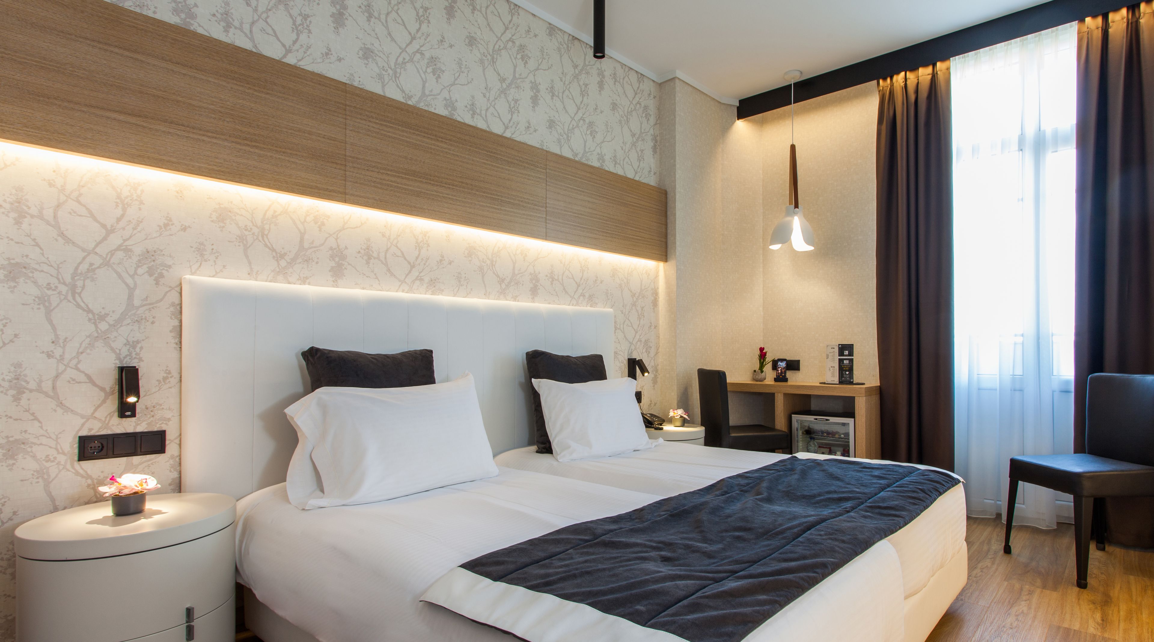 A modern hotel room with a large bed, bedside tables, a desk, and a chair.