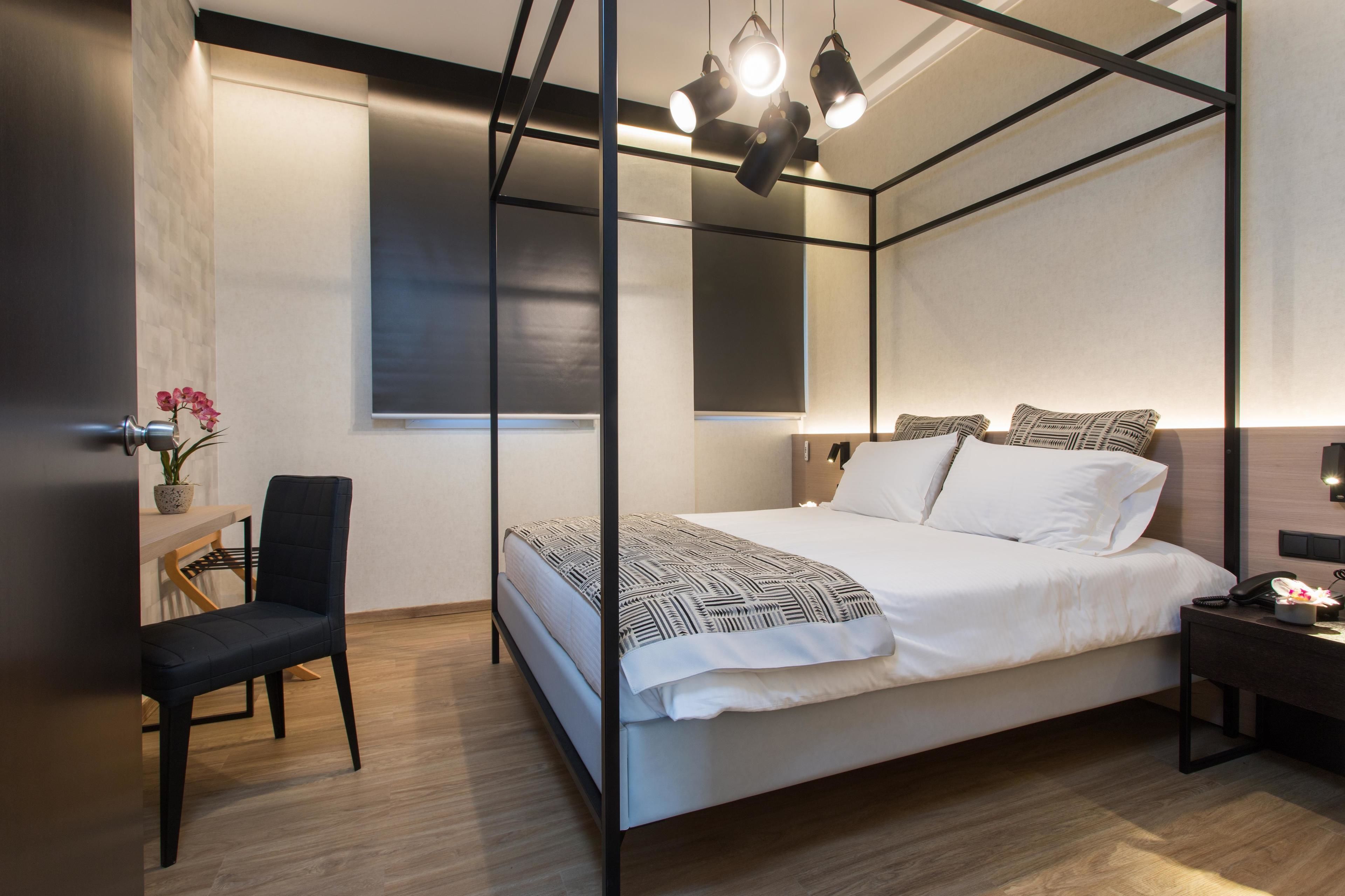 A modern bedroom with a four-poster bed, a bedside table, a chair, and a small desk with a plant.