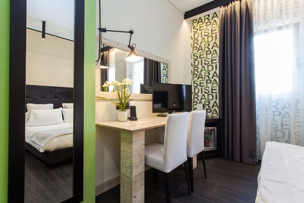 Habitación de hotel con cama, escritorio con computadora, silla, televisor y planta en maceta.