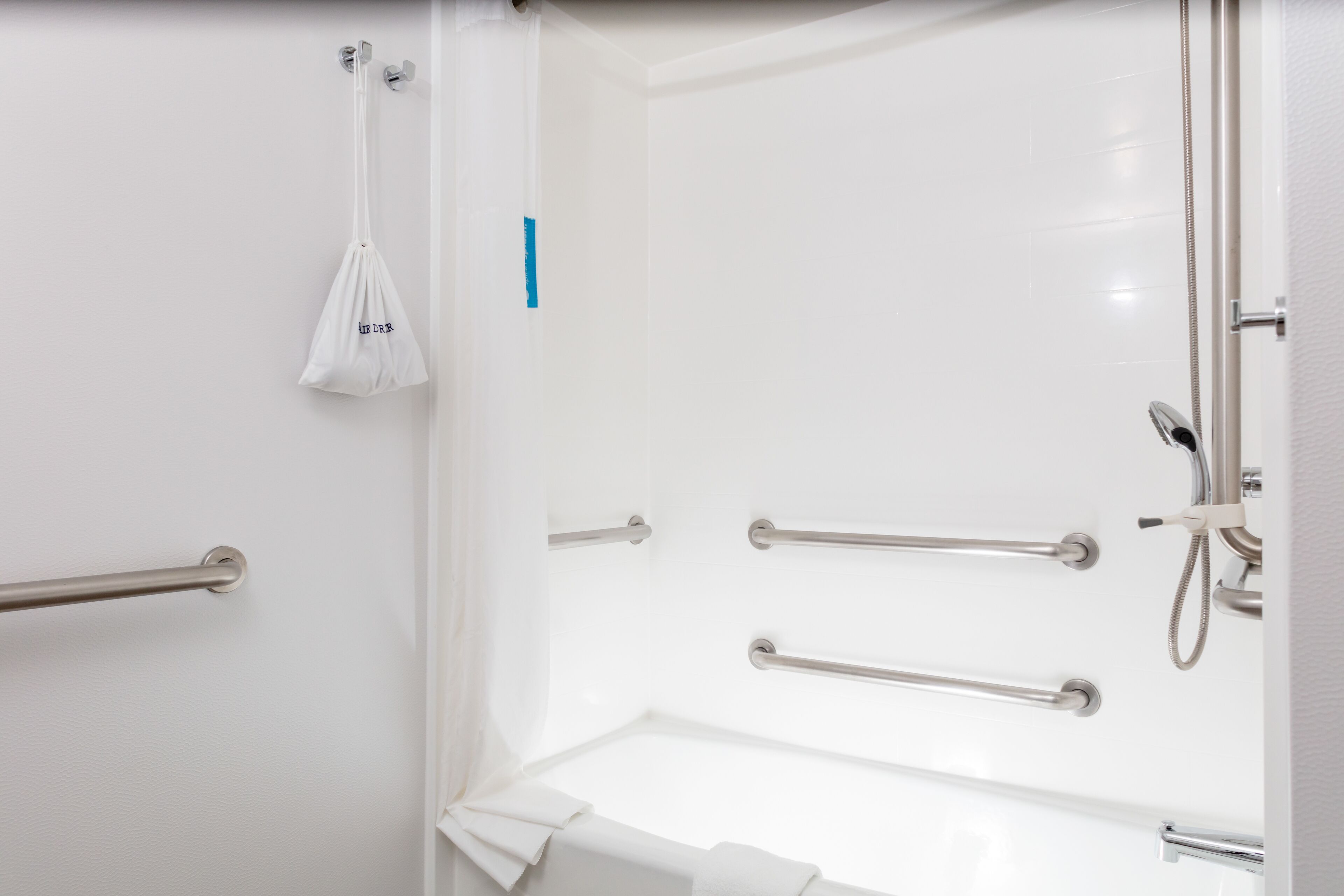 A bathroom with a white bathtub, grab bars, and a showerhead.