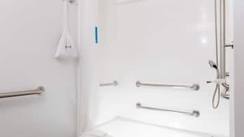 A bathroom with a white bathtub, grab bars, and a showerhead.