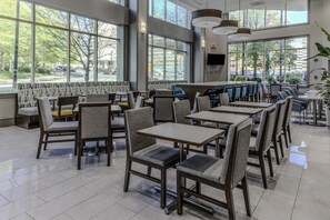 A spacious indoor seating area with multiple tables and chairs, large windows offering a view of the street, and a modern ceiling design. - Hampton Inn & Suites Arlington Crystal City DCA (Arlington)