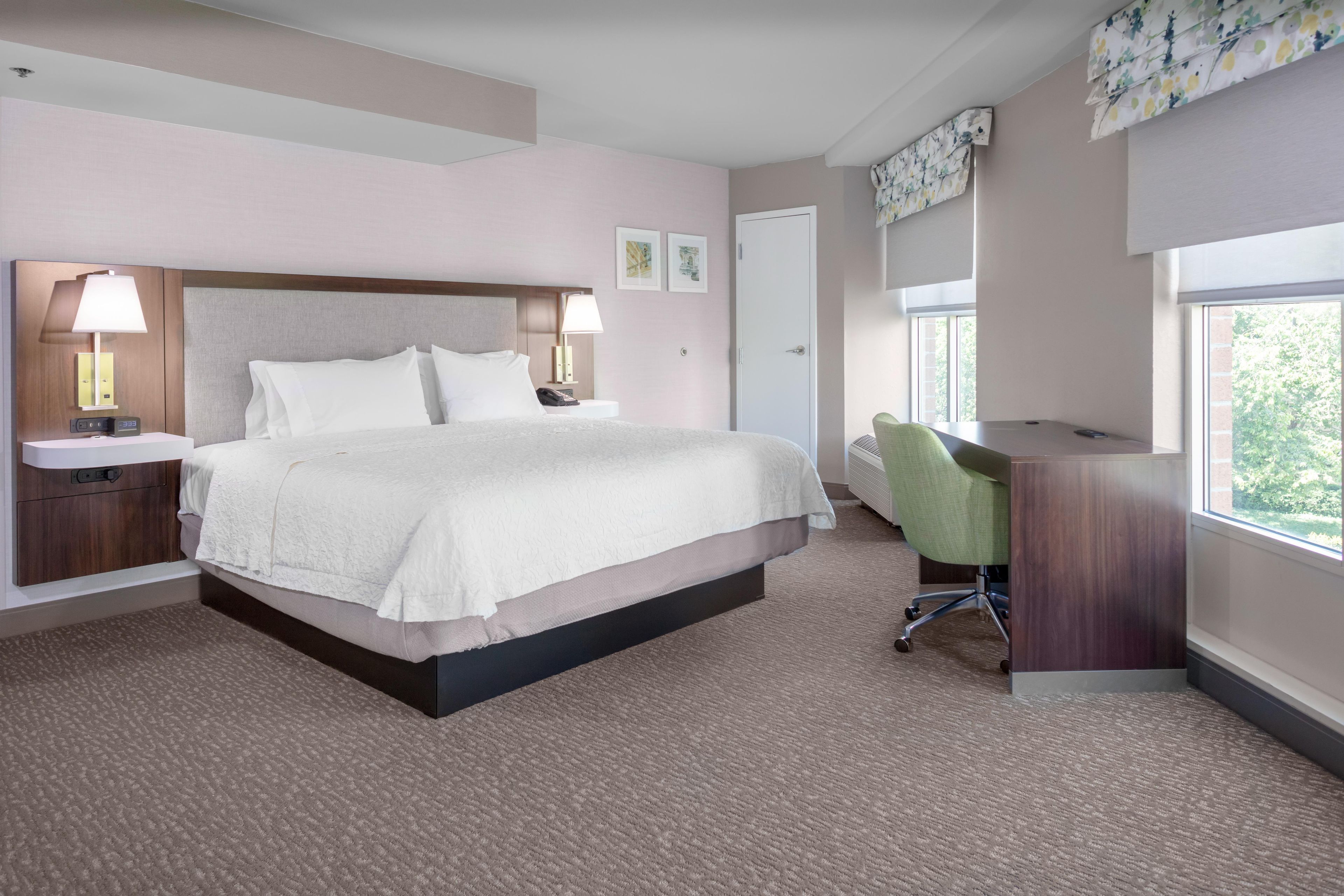 A hotel room with a large bed, bedside lamps, a desk, and a chair.