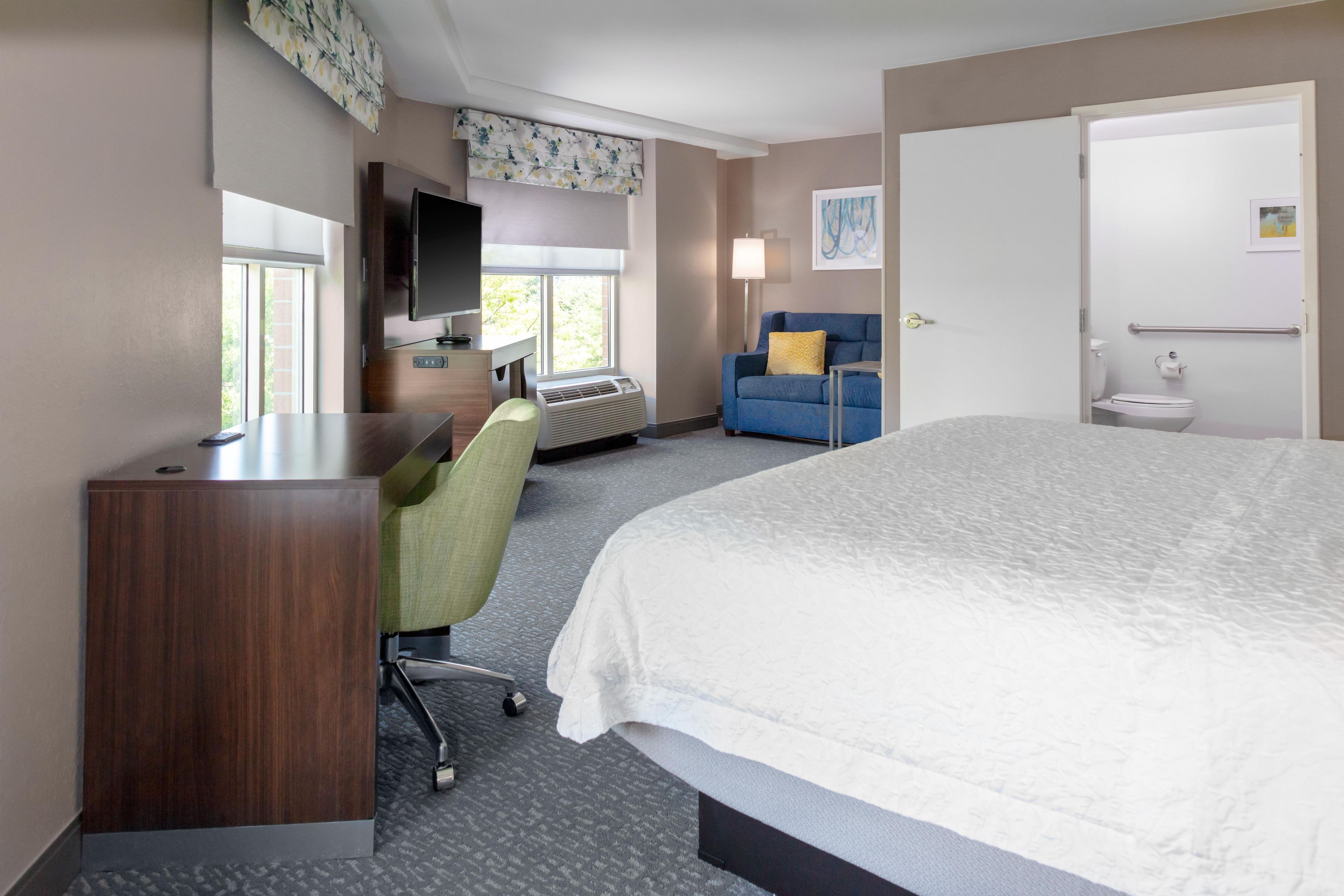 A hotel room with a bed, a desk, a chair, a television, a window, and a bathroom.