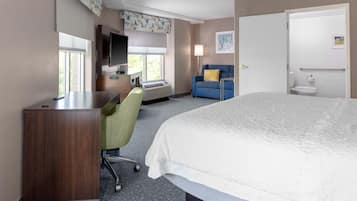 A hotel room with a bed, a desk, a chair, a television, a window, and a bathroom.