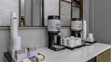 A coffee station with two coffee dispensers, stacks of disposable cups, and a variety of tea and coffee packets.
