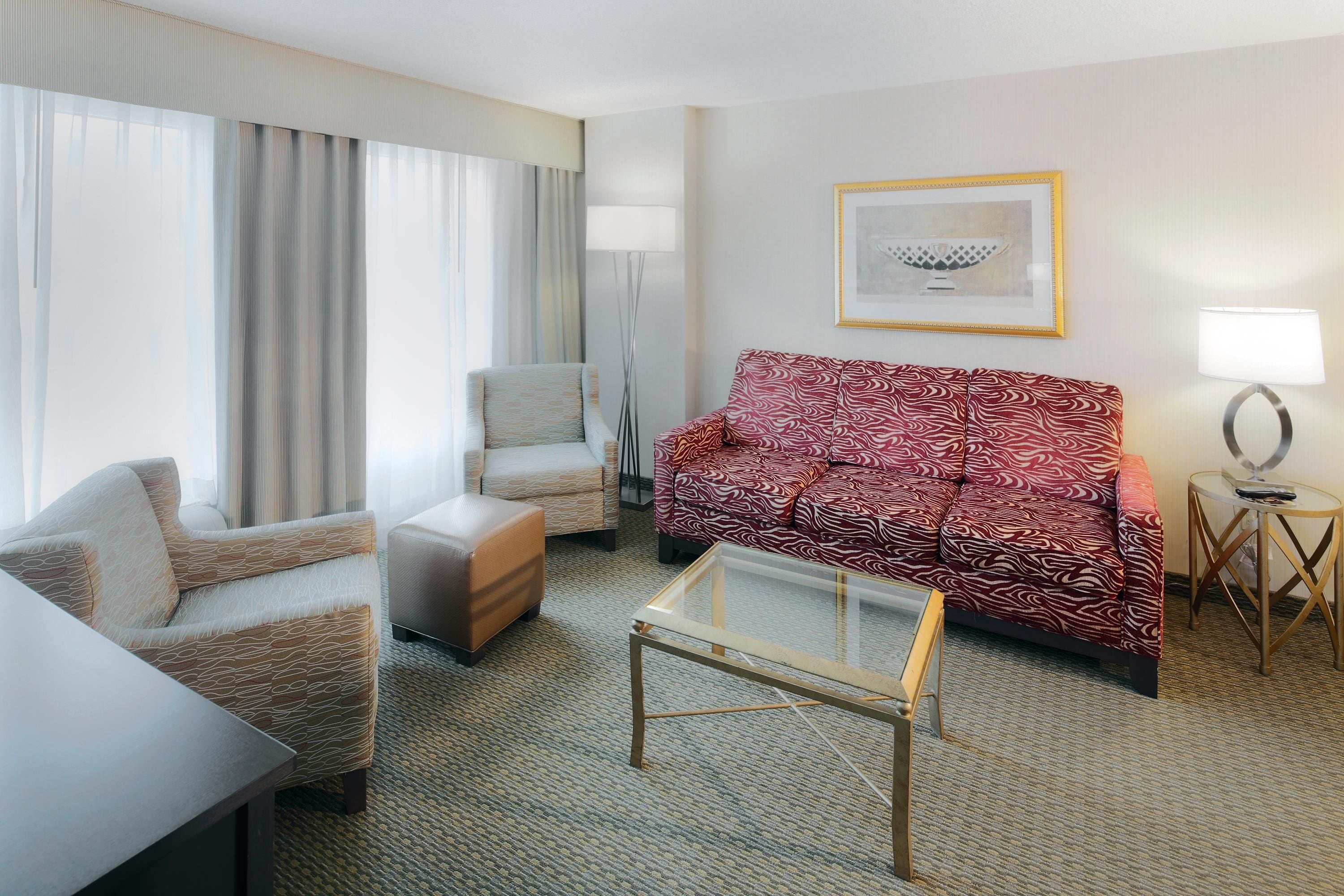 Habitación de hotel con sofá, sillón, reposapiés y una mesita de centro de vidrio.