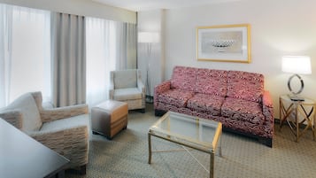 Habitación de hotel con sofá, sillón, reposapiés y una mesita de centro de vidrio.