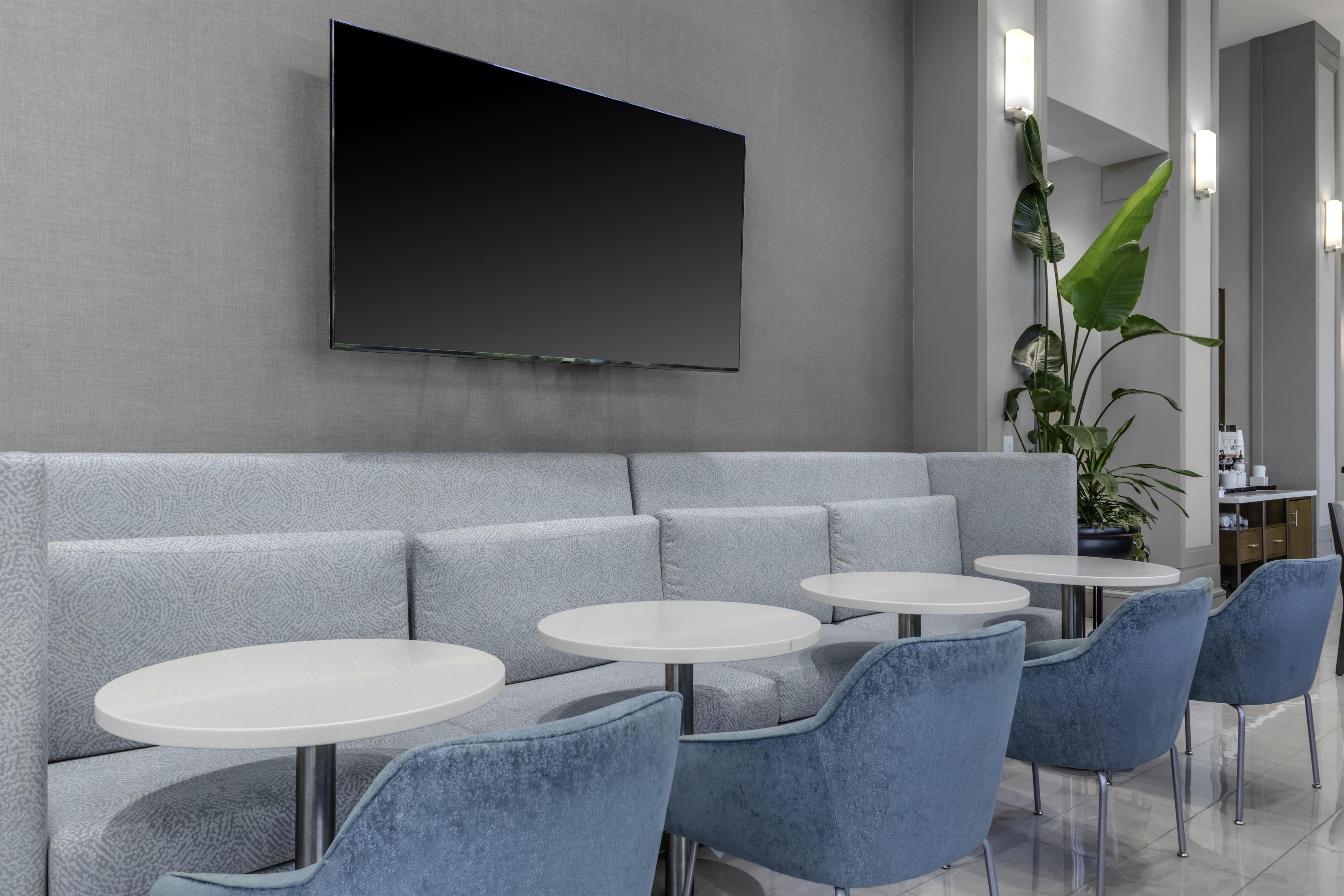 A modern lounge area with a grey sofa, white round tables, and blue chairs.