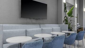 A modern lounge area with a grey sofa, white round tables, and blue chairs.