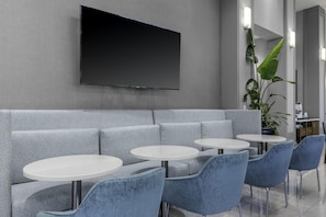 A modern lounge area with a grey sofa, white round tables, and blue chairs. - Hampton Inn & Suites Arlington Crystal City DCA (Arlington)