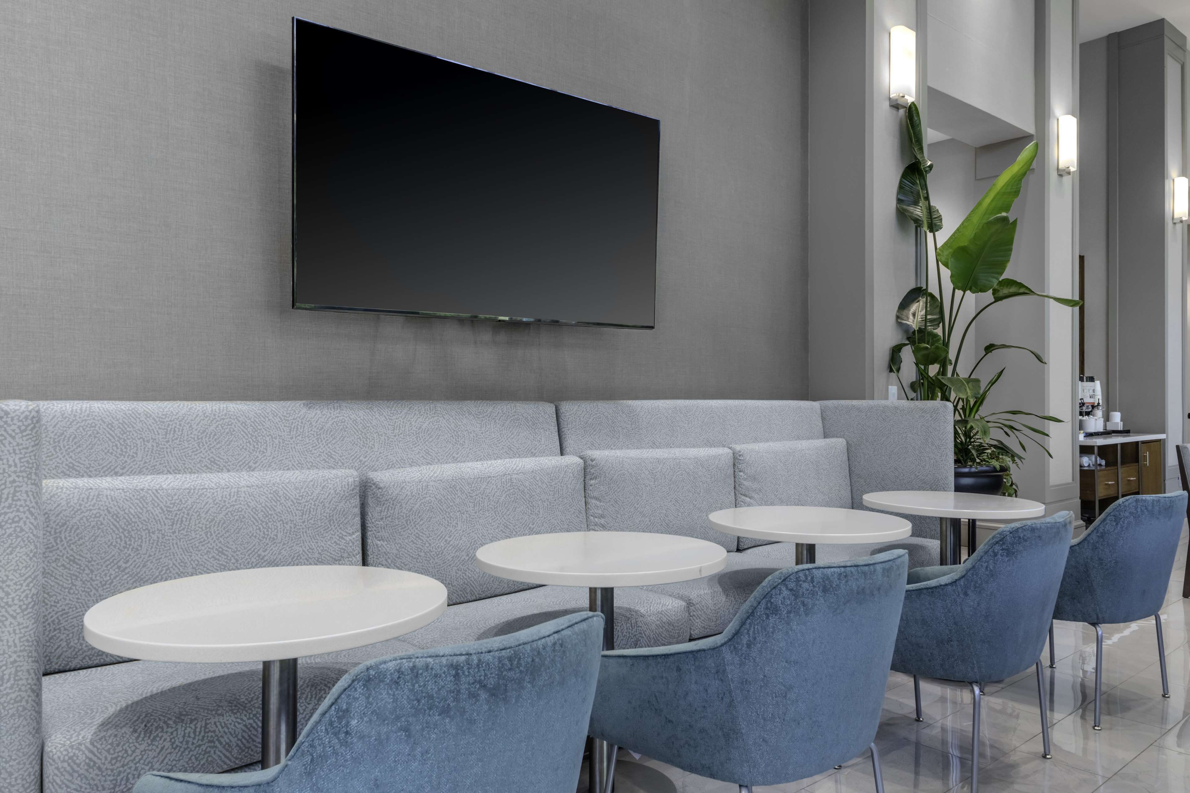 A modern lounge area with grey upholstered seating, round white tables, and blue chairs.
