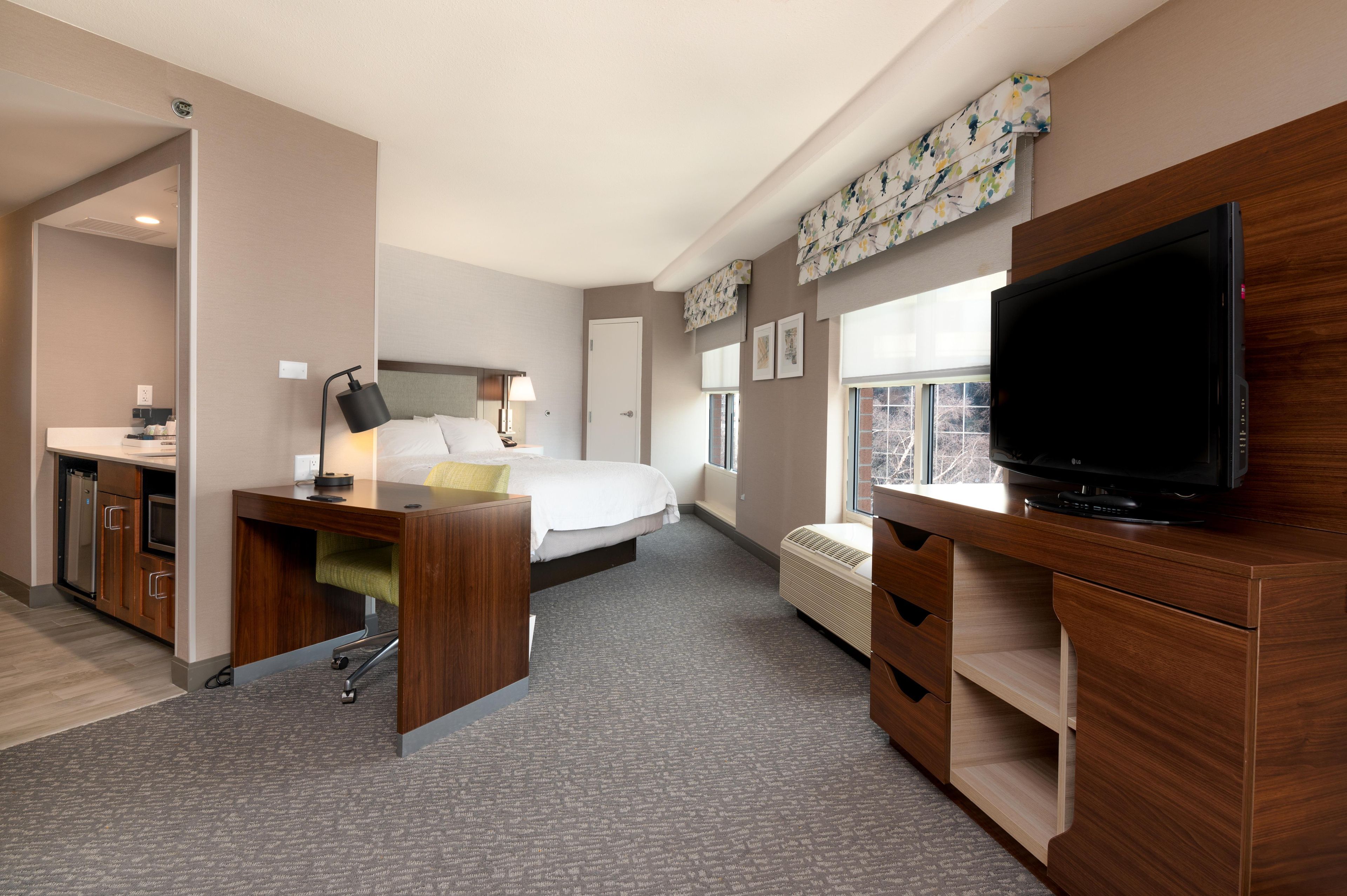 Una habitación de hotel con cama, escritorio con lámpara, televisor y ventana con persianas.