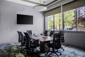 A conference room with a large table, chairs, a flat-screen TV, and a view of trees and buildings through large windows. - Hampton Inn & Suites Arlington Crystal City DCA (Arlington)