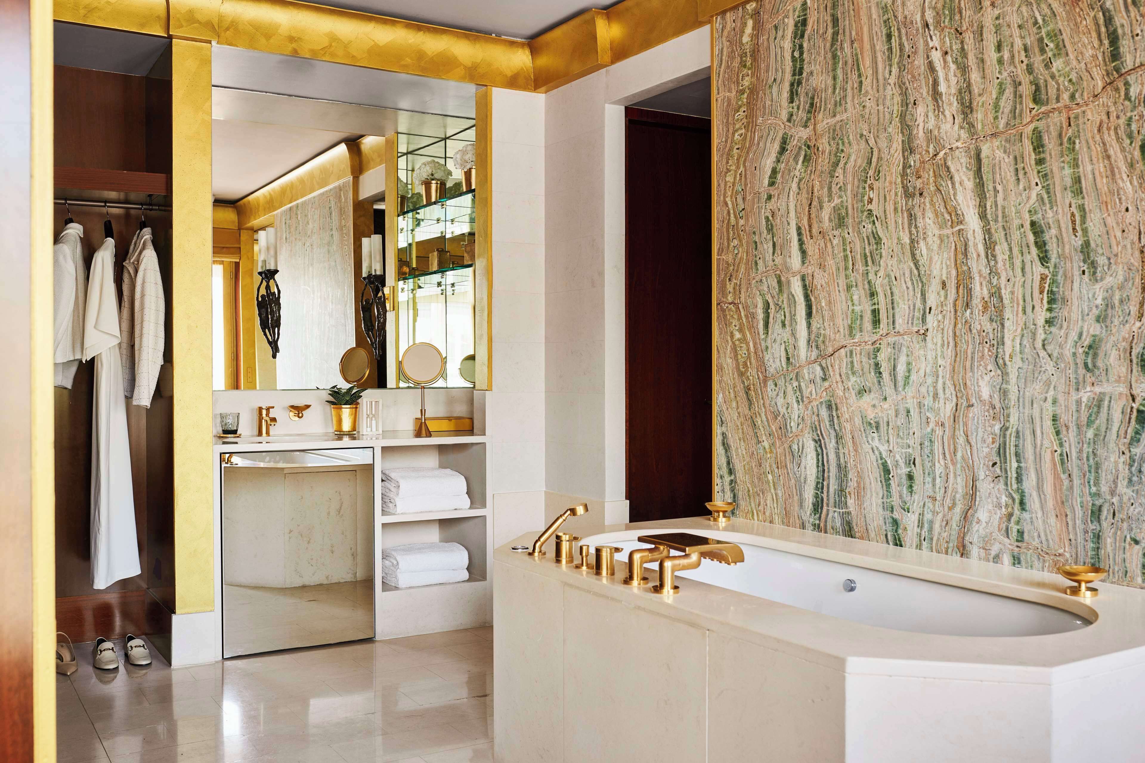 A modern bathroom with a large bathtub, a vanity with gold fixtures, and a marble wall.