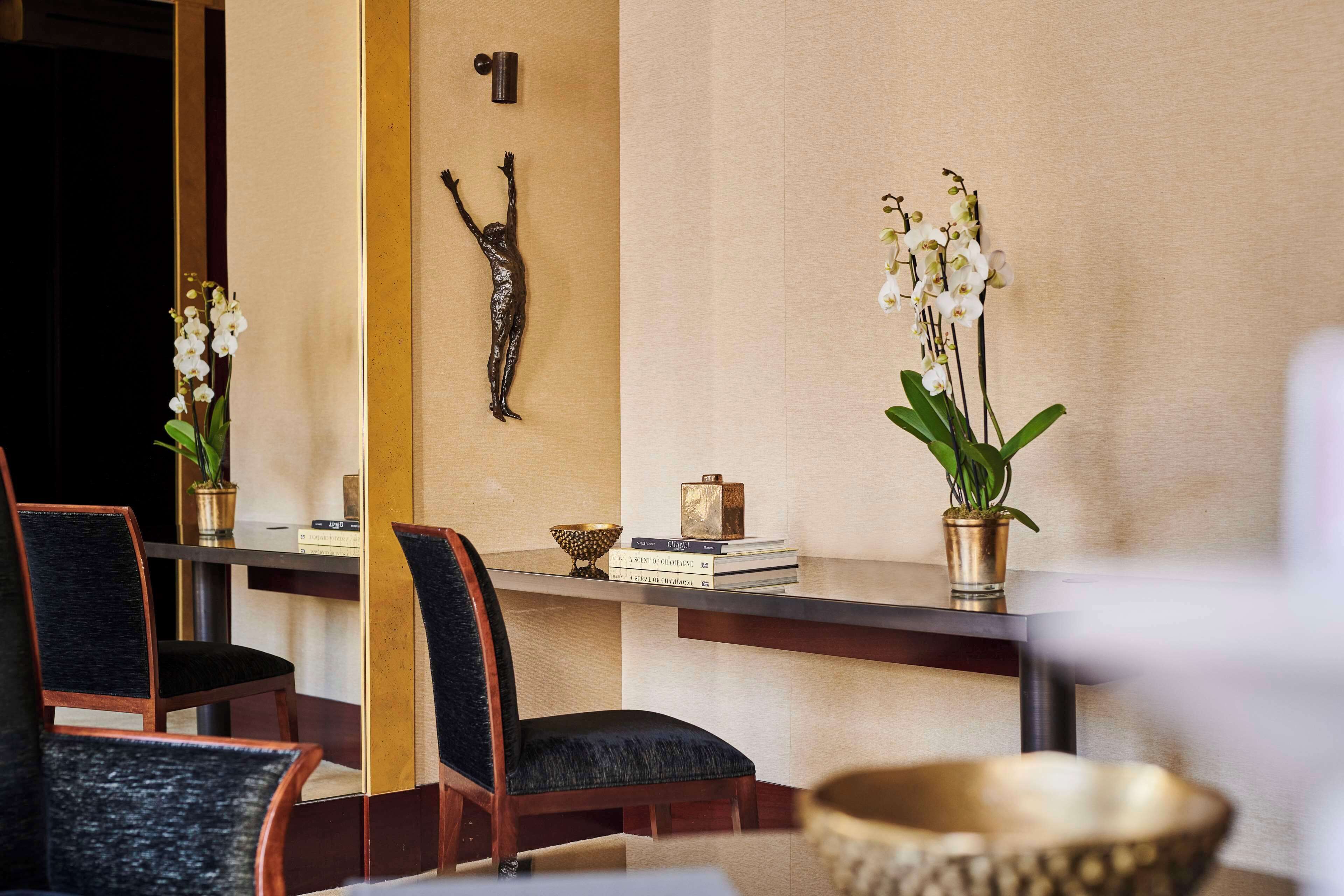 A modern interior with a wooden reception desk, chairs, and decorative items including orchids and a sculpture.