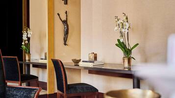 A modern interior with a wooden reception desk, chairs, and decorative items including orchids and a sculpture.
