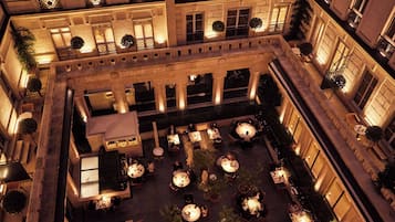 A courtyard with multiple tables and chairs, surrounded by buildings with balconies and windows.