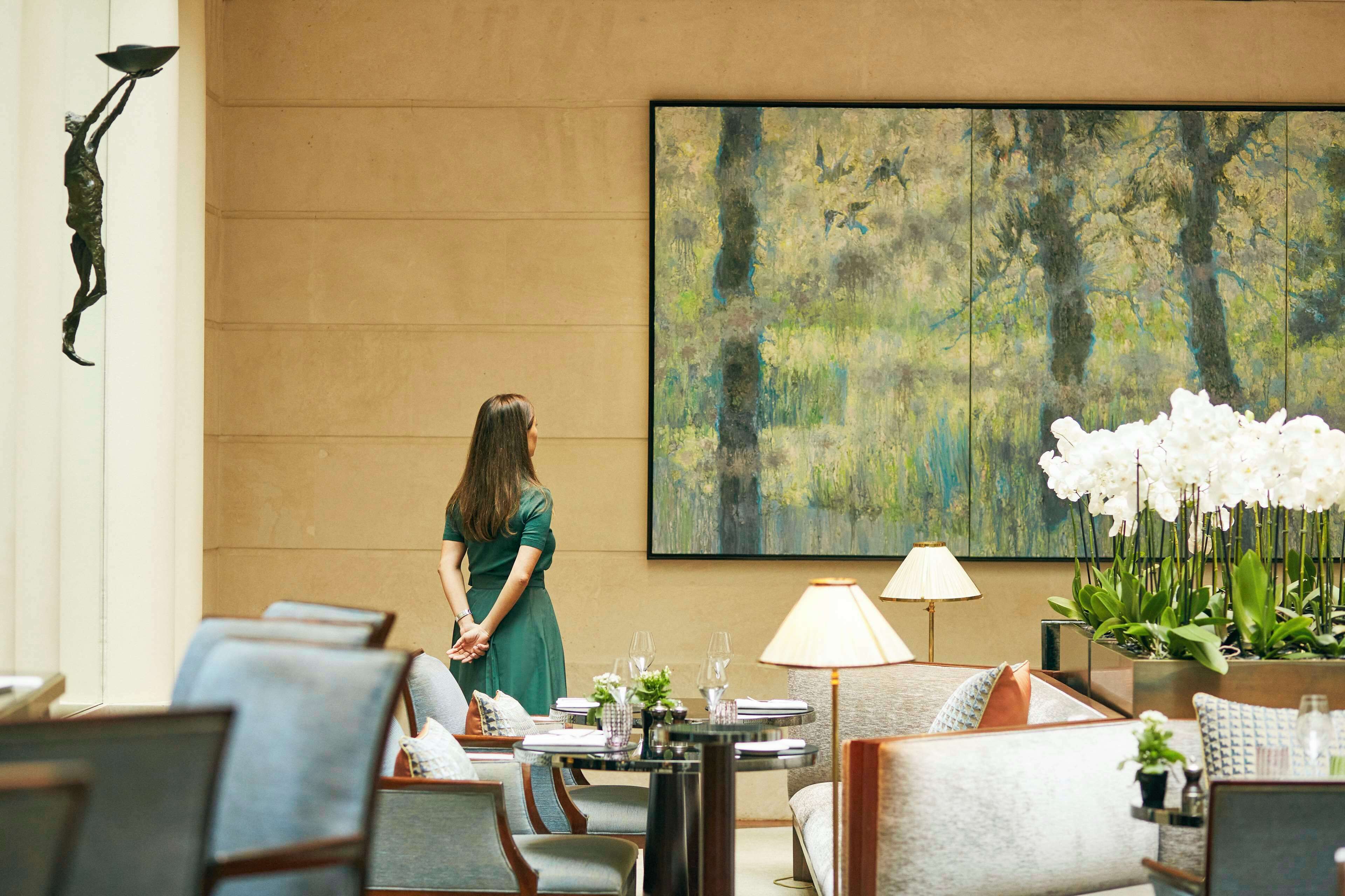 A hotel lobby with a large abstract painting, seating arrangements, and a potted plant with white flowers.