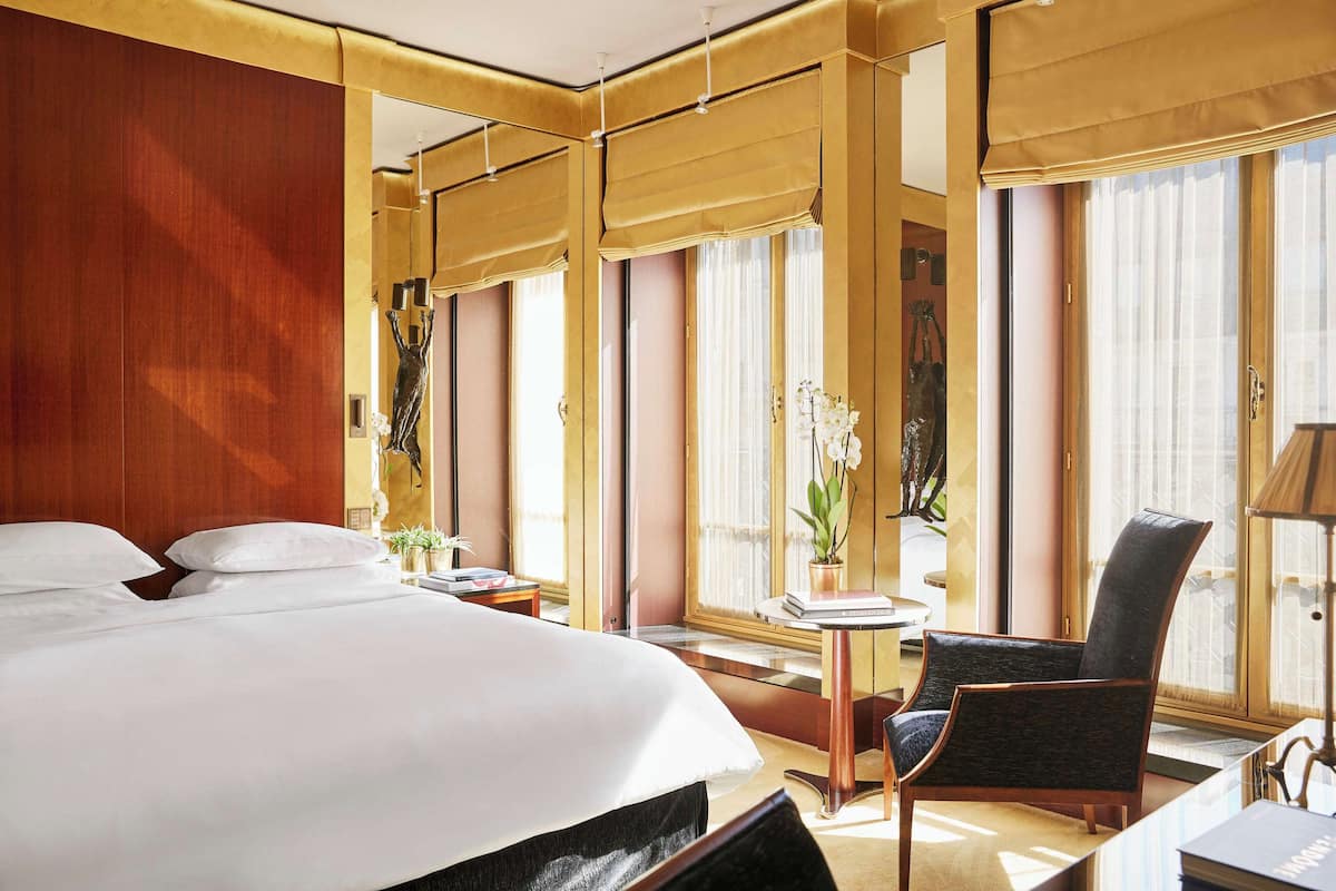 Ein Hotelzimmer mit einem großen Bett, einem Sessel, einem kleinen Tisch und einem Fenster mit Vorhängen.