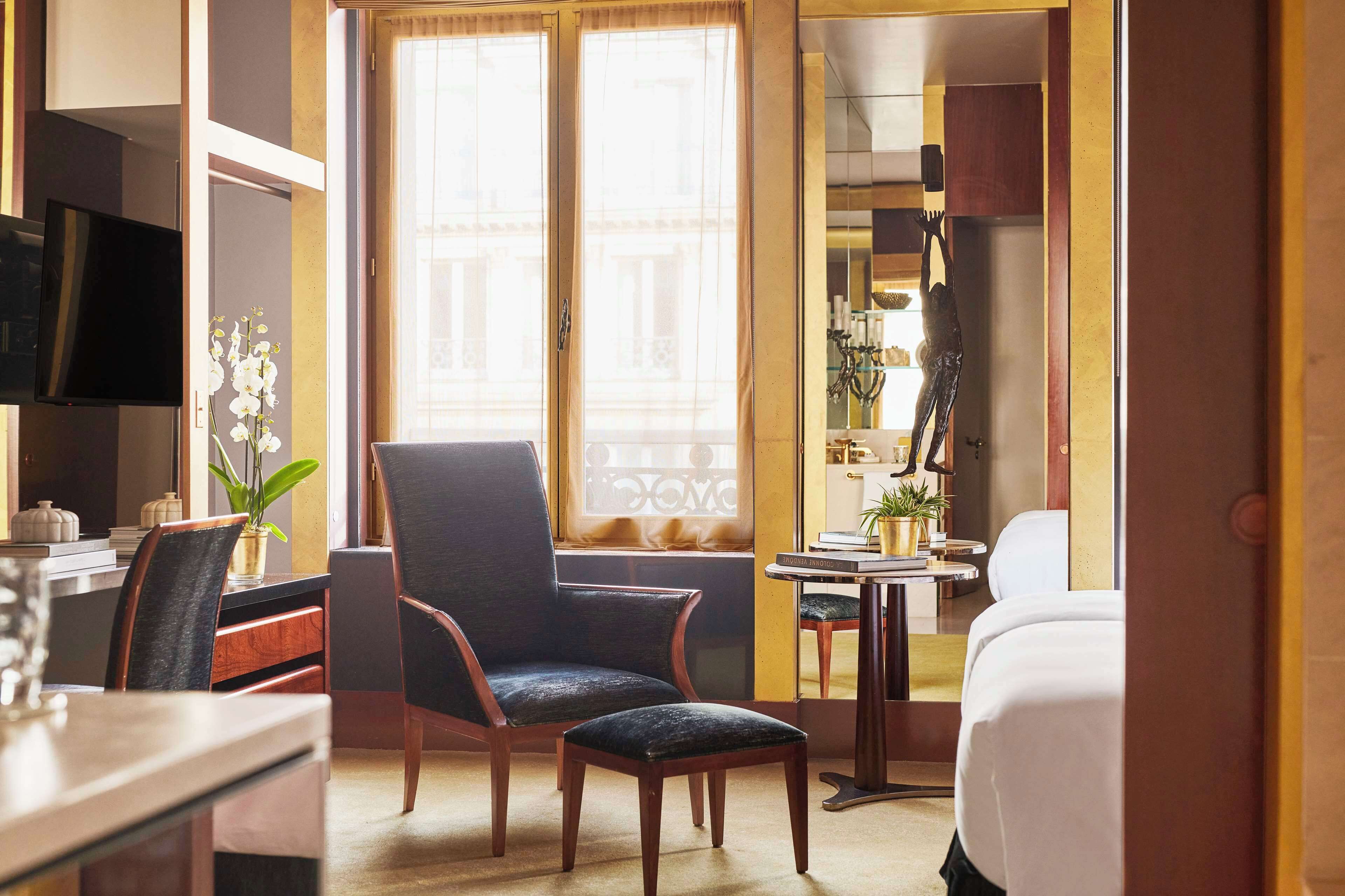 A hotel room with a desk, a chair, a bed, and a small table with a plant.