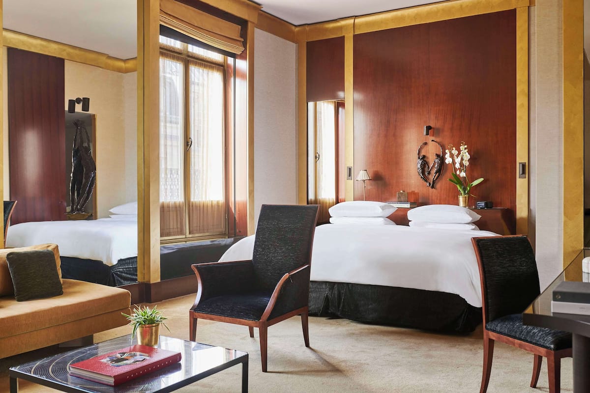 Ein Hotelzimmer mit zwei Betten, einer Sitzecke mit einer Couch und Sesseln, einem kleinen Tisch mit einem Buch und einer Zimmerpflanze.