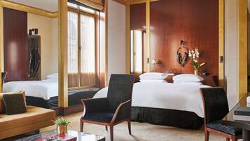 Une chambre d’hôtel avec deux lits, un coin salon avec un canapé et des fauteuils, une petite table avec un livre et une plante décorative.