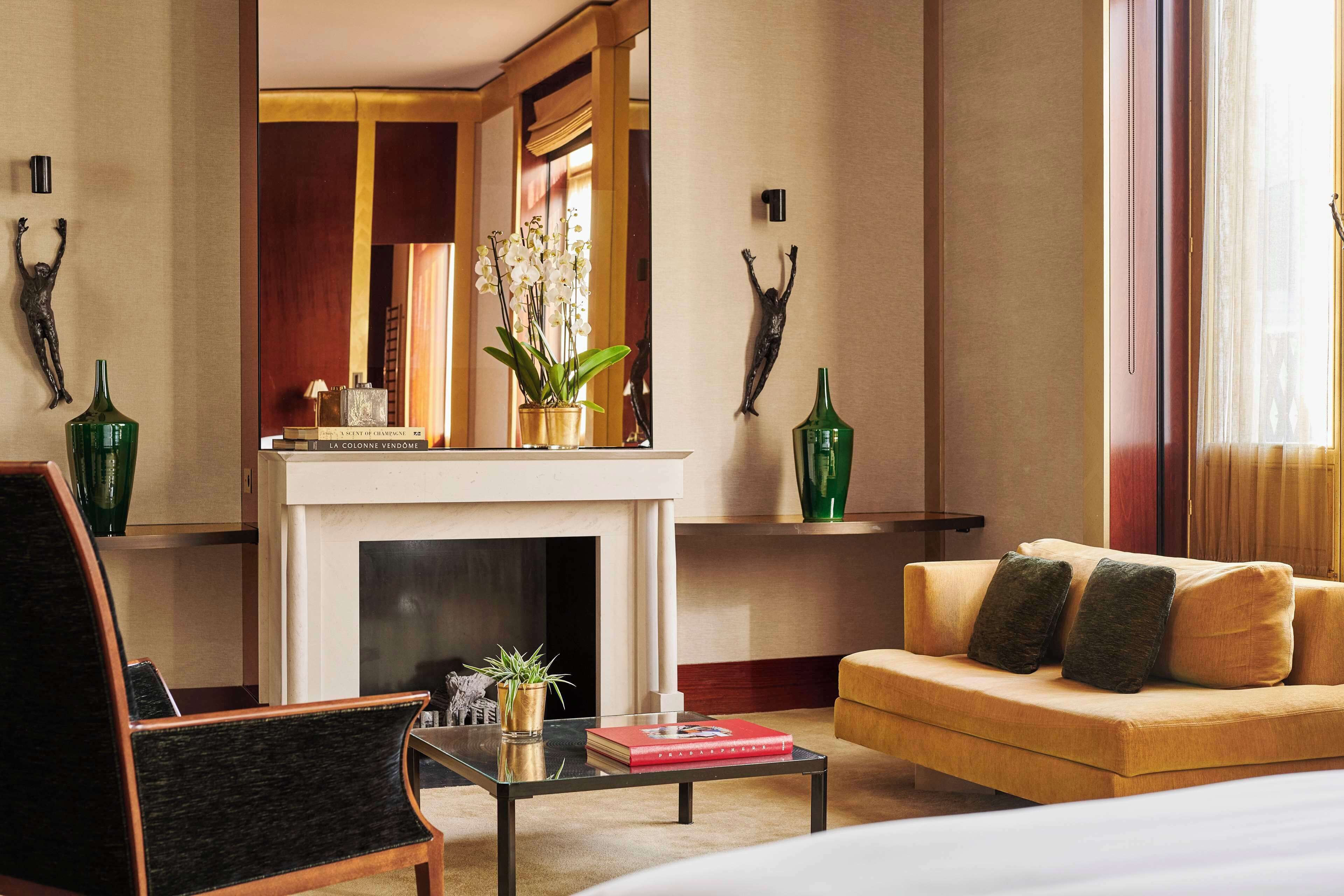 Une chambre d’hôtel moderne, dotée d’un canapé, d’une table basse, d’une cheminée et d’objets décoratifs, notamment un crucifix et des vases.
