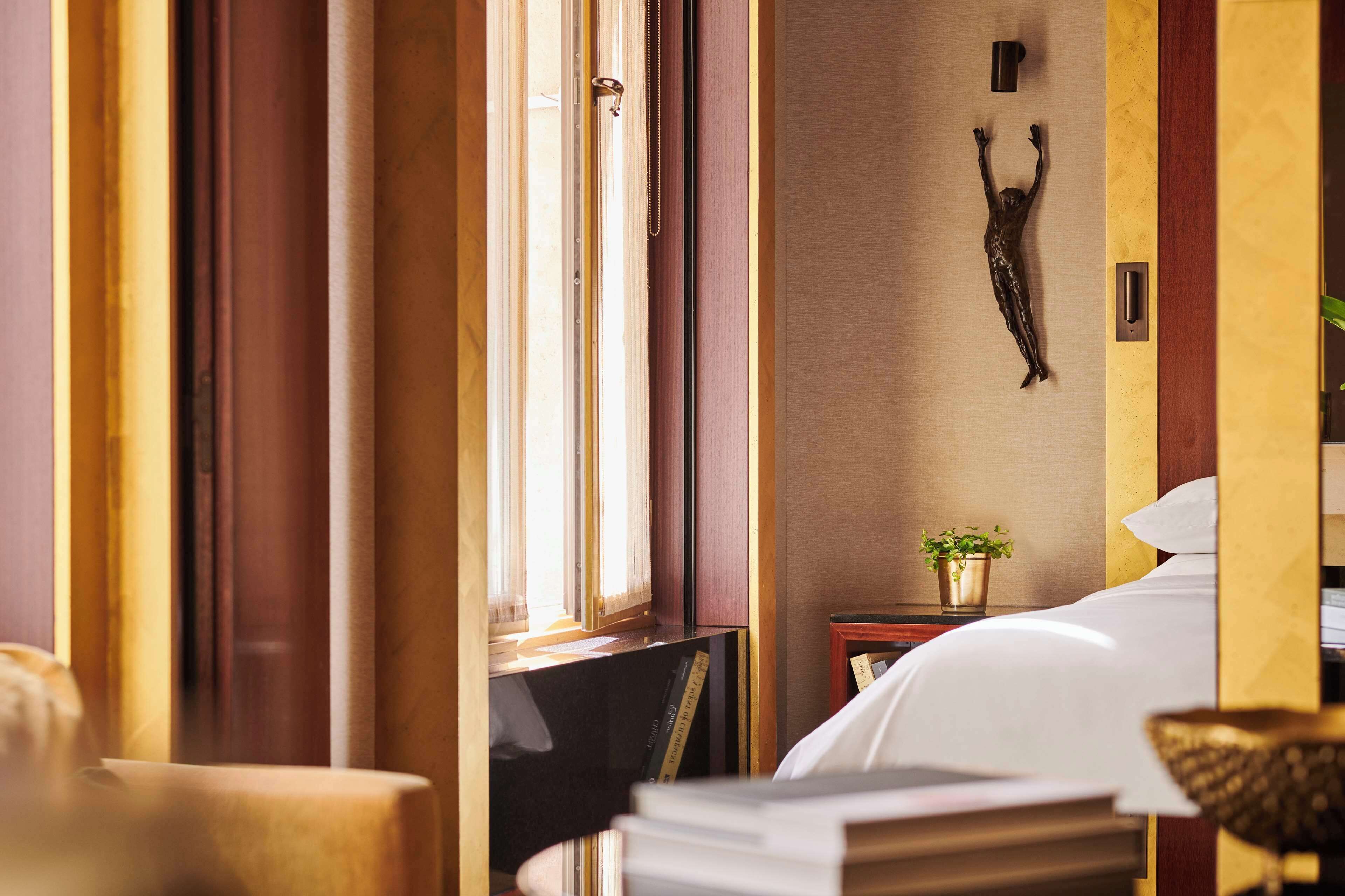 A hotel room with a bed, a small table with a plant, and a wall-mounted sculpture.