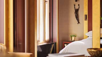 A hotel room with a bed, a small table with a plant, and a wall-mounted sculpture.