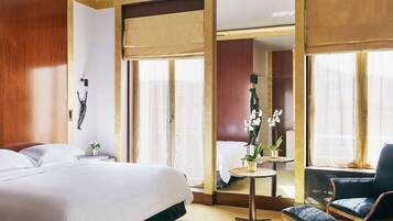 Habitación de hotel con una cama grande, una mesita con una planta, una silla y vistas a otra habitación a través de una puerta corredera.
