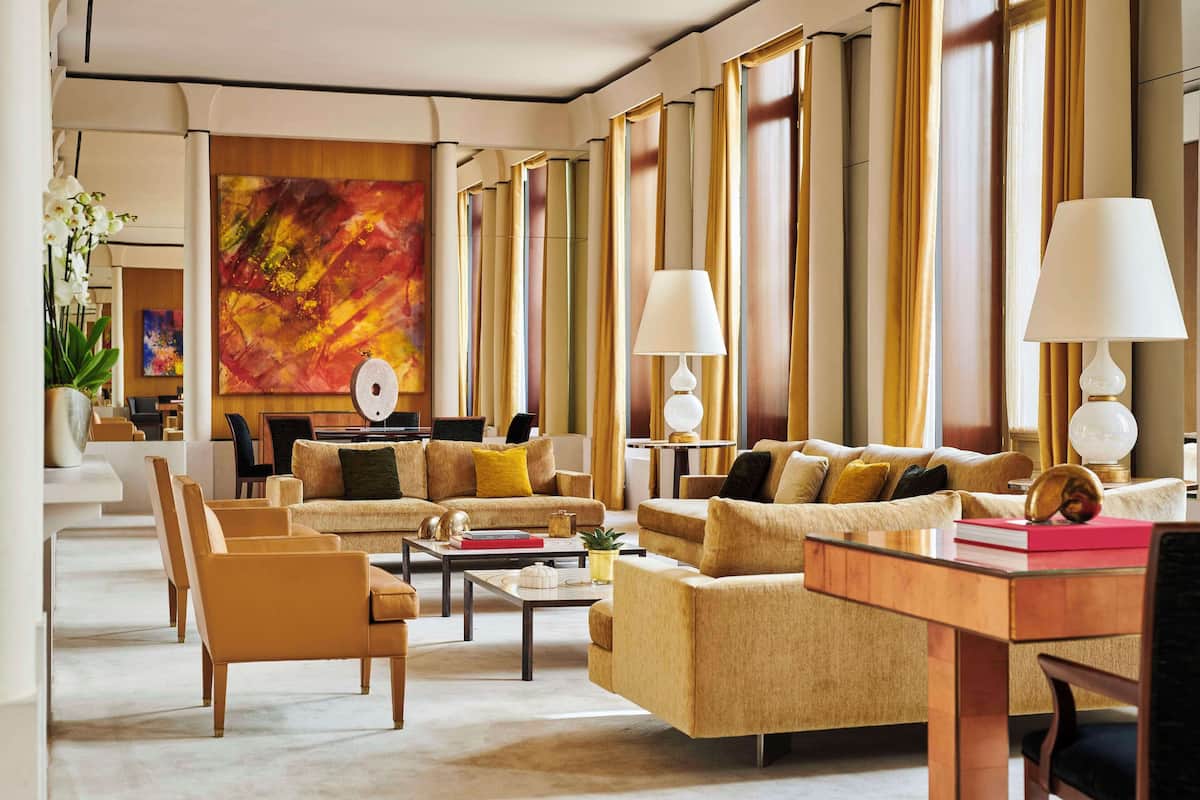 Ein geräumiges Wohnzimmer mit mehreren Sofas, einem Couchtisch und Lampen. An der Wand hängt ein großes abstraktes Gemälde und links steht ein Blumentopf.