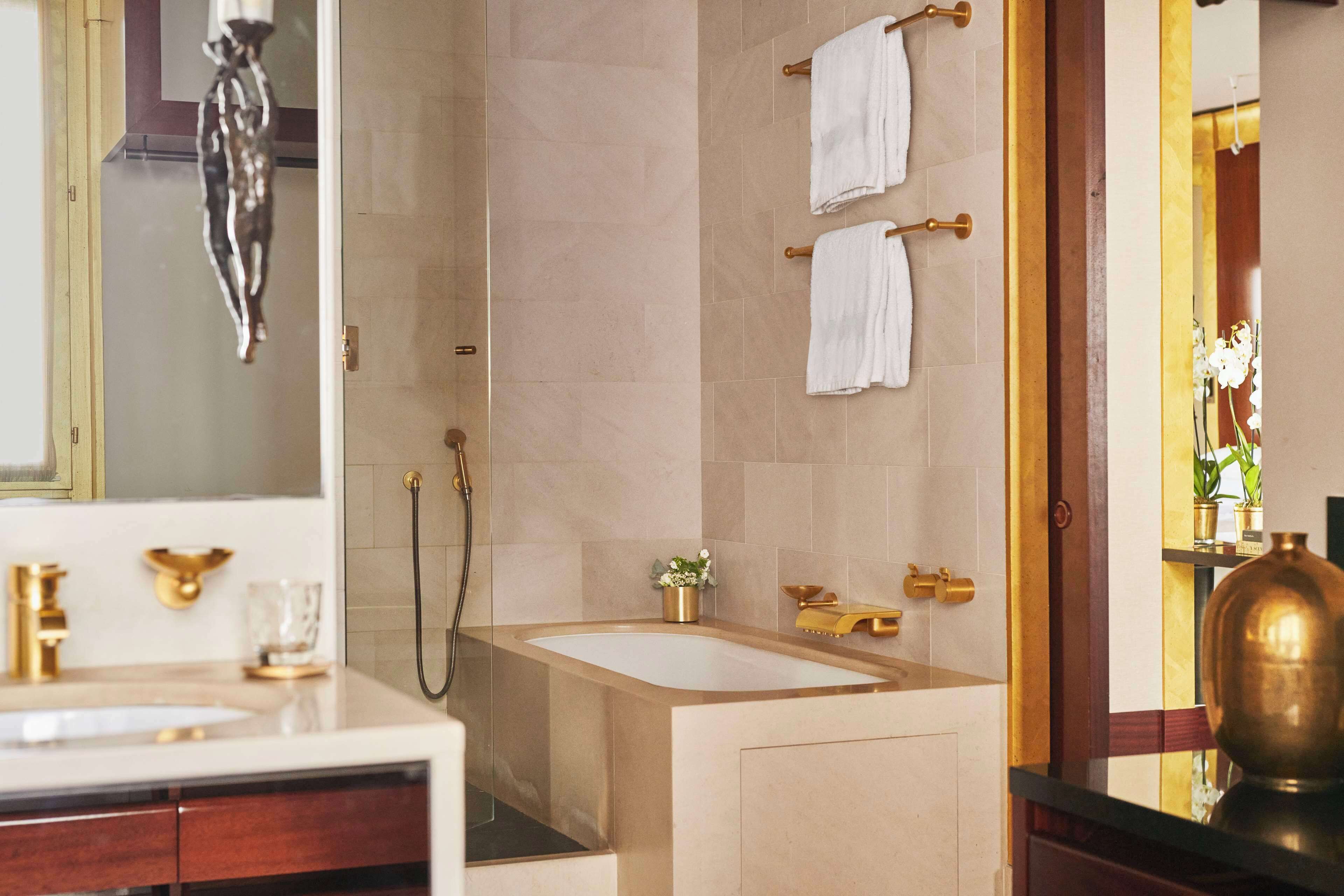 A modern bathroom with a large bathtub, a vanity with a gold faucet, and two towels hanging on a towel rack.