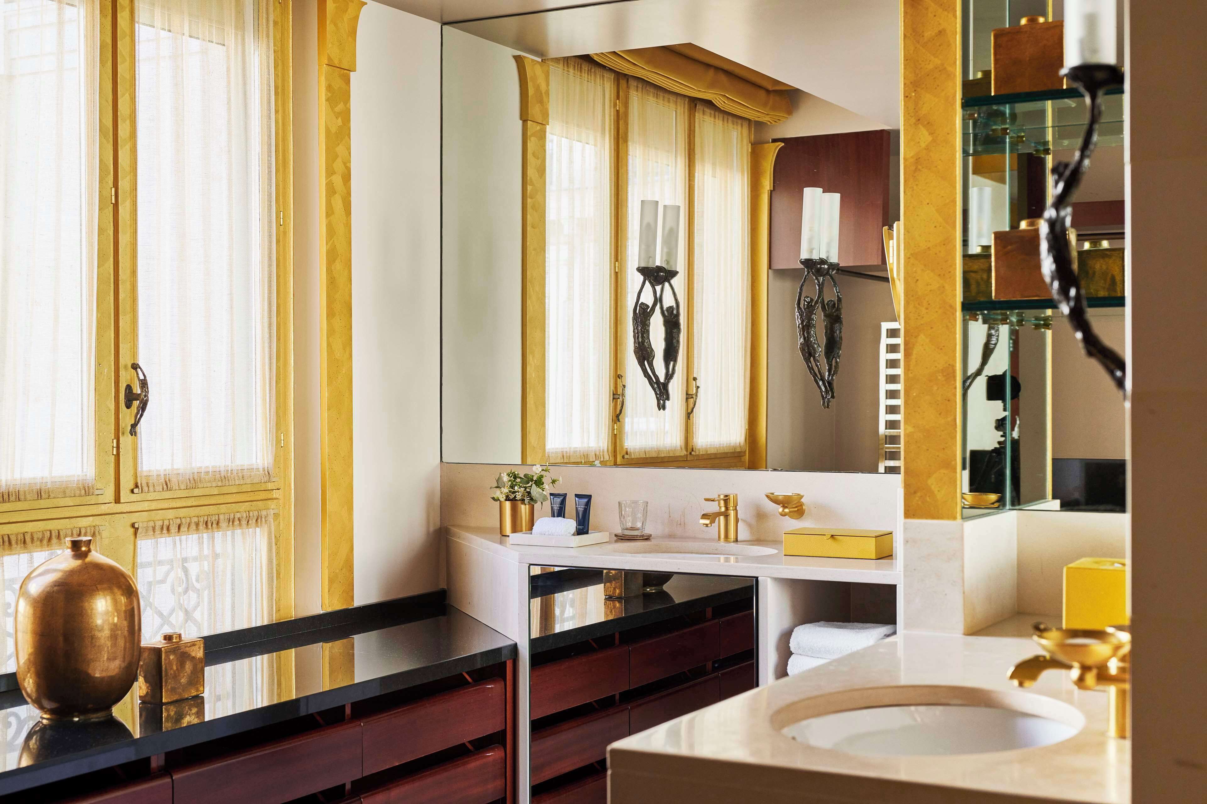 A bathroom with a large mirror, a white sink, and a vanity with a gold-colored cabinet.