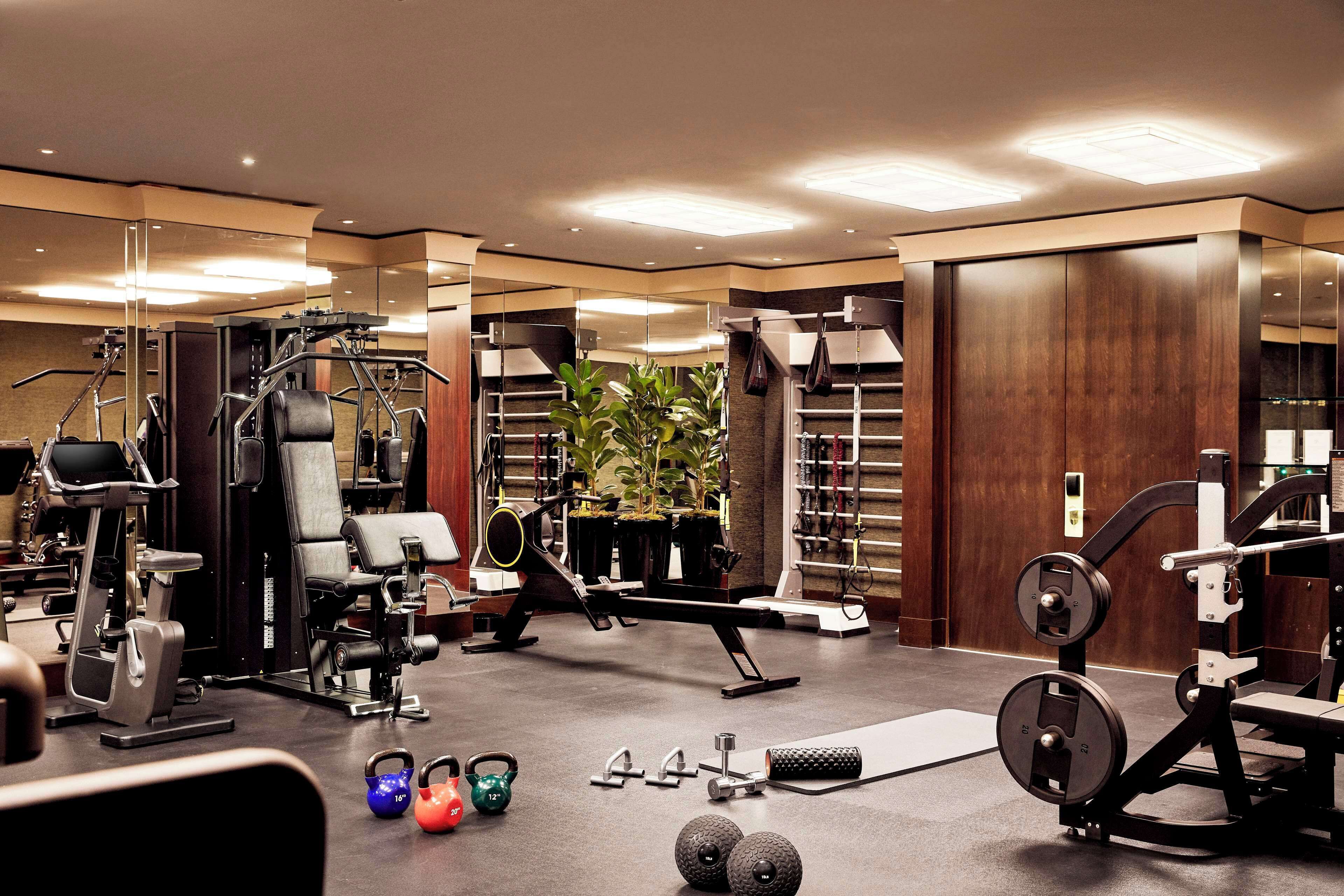 Un gimnasio bien equipado con diversas máquinas de ejercicio, pesas y kettlebells.
