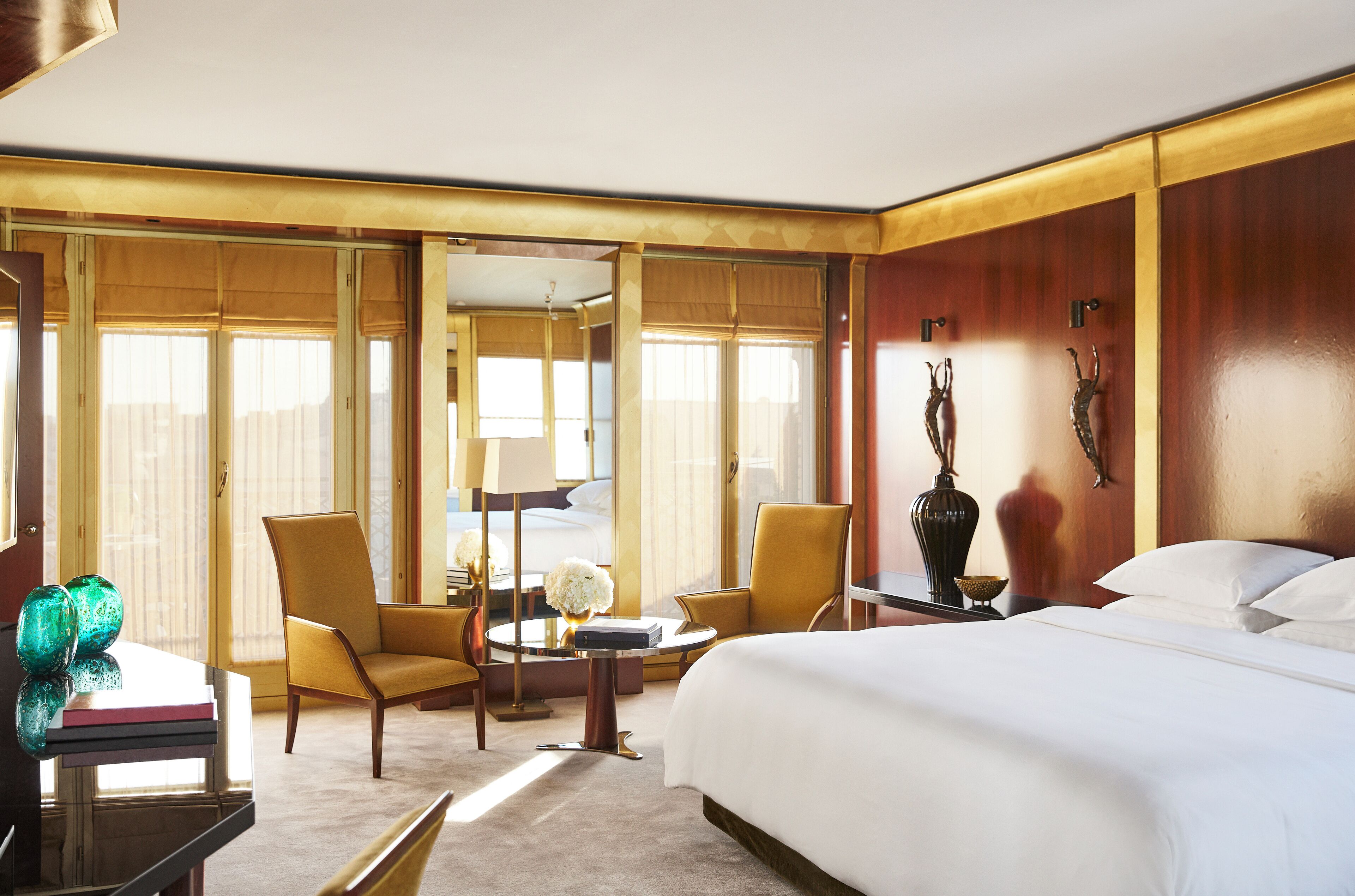 A hotel room with a large bed, two armchairs, a small table, and a mirror.