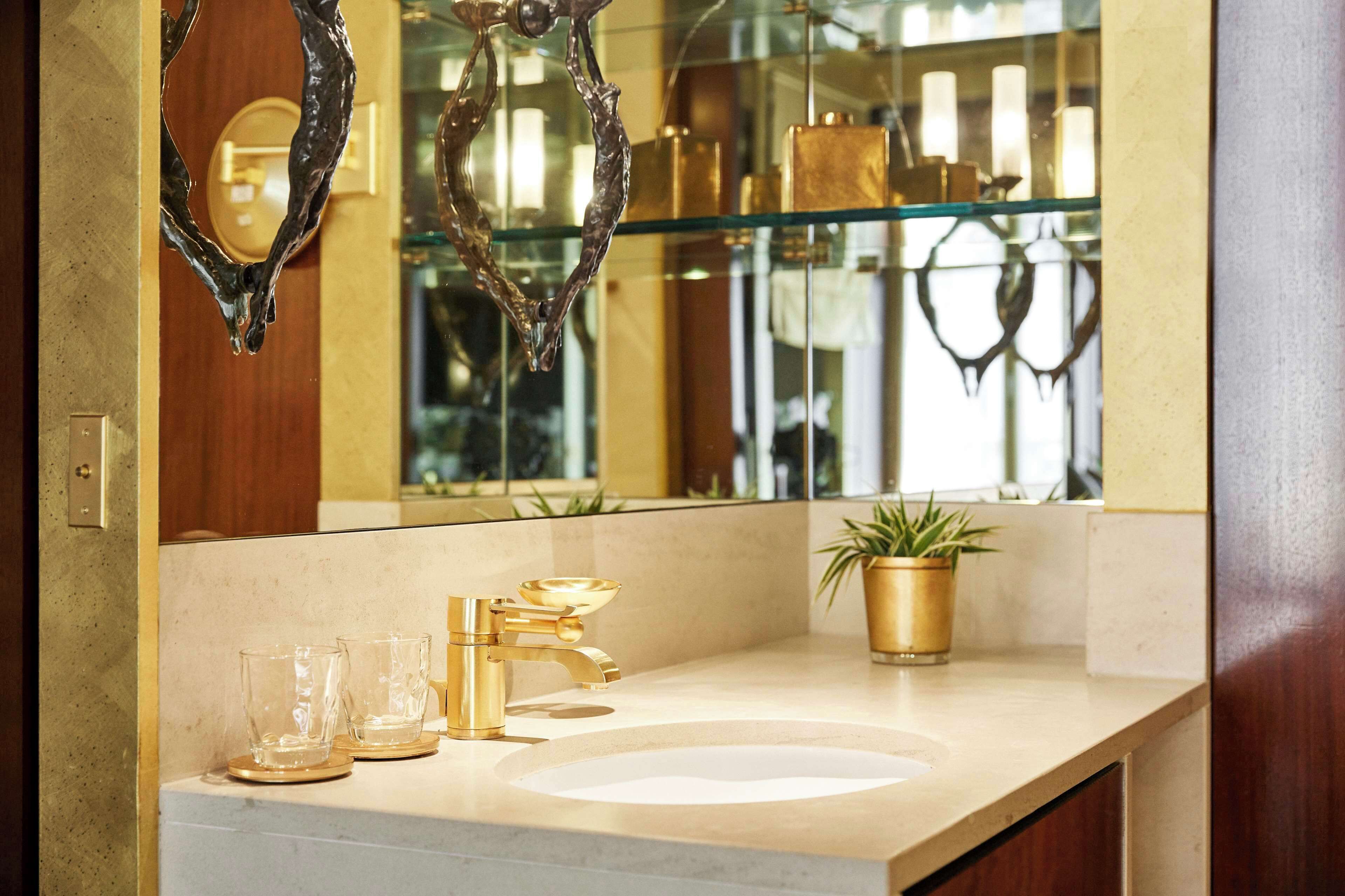 A bathroom with a gold faucet, a white sink, and a gold vase on the counter.