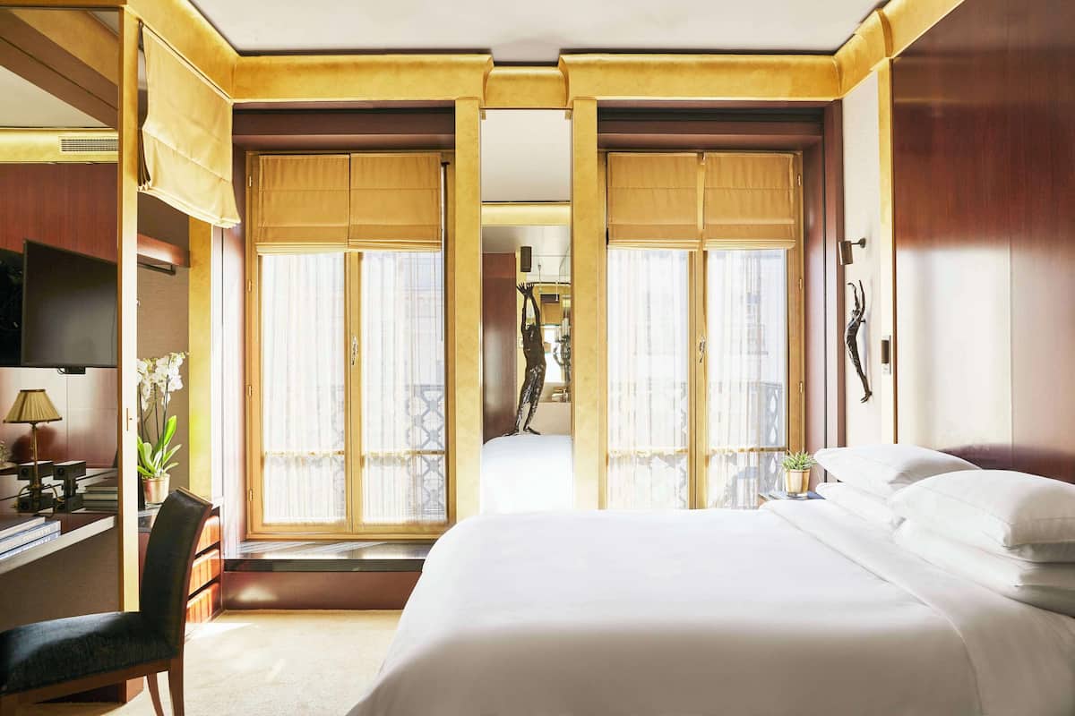 Ein Hotelzimmer mit Bett, Schreibtisch mit Lampe, Stuhl und einem Fenster mit Vorhängen.