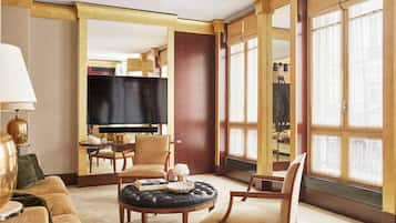 A hotel room with a large flat-screen TV, a round coffee table, a sofa, and a dining area with a table and chairs.