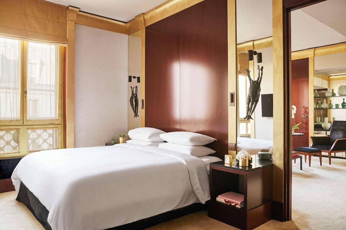 Ein Hotelzimmer mit einem großen Bett, einem Nachttisch, einem Spiegel und Blick auf das angrenzende Zimmer.