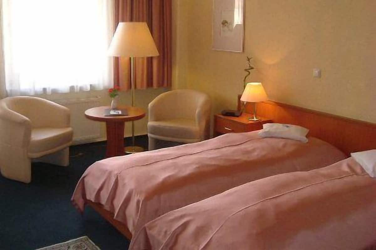 A hotel room with two beds, a sitting area with a table and chairs, and a lamp on the nightstand.
