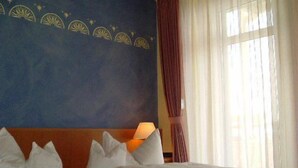 A hotel room with a large bed, a headboard with a decorative panel, a nightstand with a lamp, and a window with curtains. - Hotel & City Appartements Rothenburger Hof (Dresden)