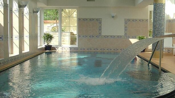 An indoor swimming pool with a clear blue water feature, white chairs, and a tiled floor. - Hotel & City Appartements Rothenburger Hof (Dresden)