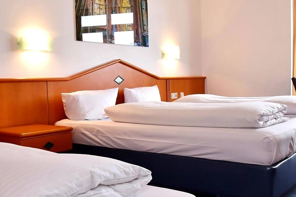 A hotel room with two beds, a wooden headboard, and a painting of a building on the wall.